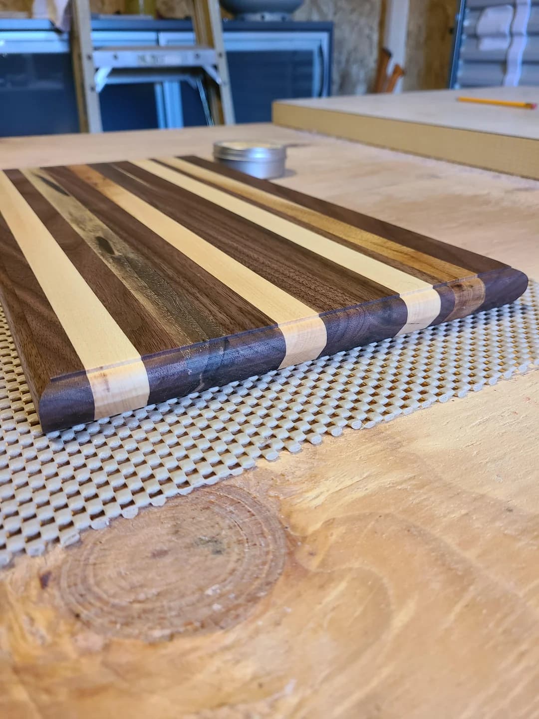 Striped walnut and maple edge-grain cutting board on the bench